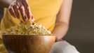 close-up woman's hand grabbing popcorn, concept of inflammatory foods that cause belly fat